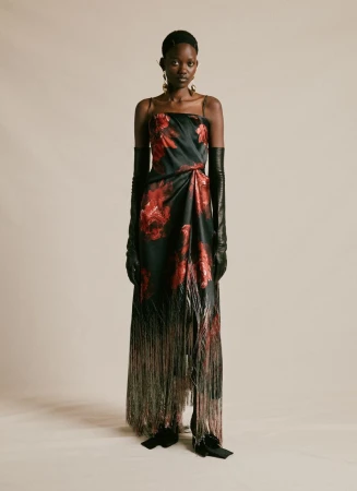 Black model standing in a black and red floral print strapless dress with long fringe hem and black opera gloves against a beige backdrop.