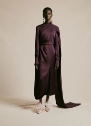 Model in plum satin dress with long cape and feathered shoes against a neutral background