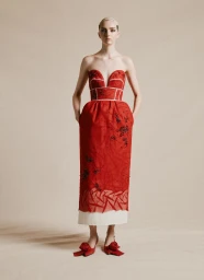 Model in a strapless red midi dress with white piping and matching rosette heels against a neutral studio backdrop.