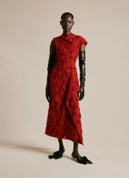 Model in red textured dress wearing long black gloves and black slingback shoes against a plain neutral background