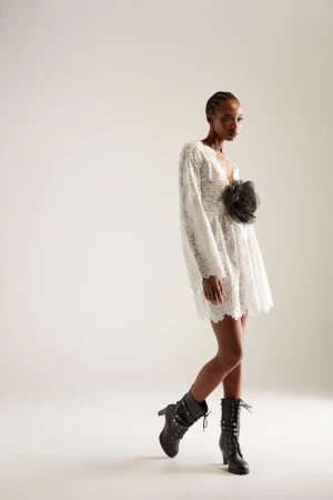 Woman in eyelet mini dress with puffed sleeves and combat boots in a fashion studio portrait against a neutral background.