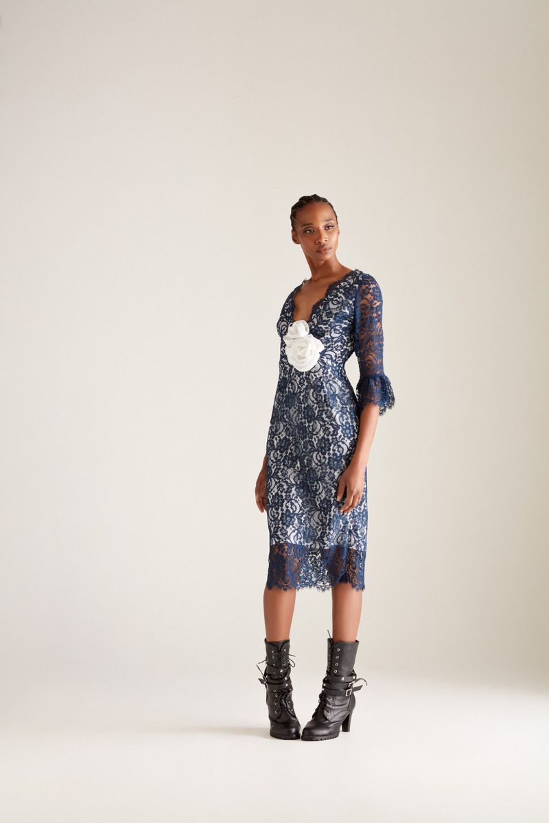 Full-length shot of a Black female fashion model in a blue lace dress with black heeled boots against an off-white studio backdrop.