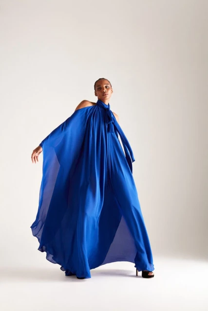 Fashion photo of a woman in a royal blue, flowing gown with bare shoulders and black platform heels against a neutral background.