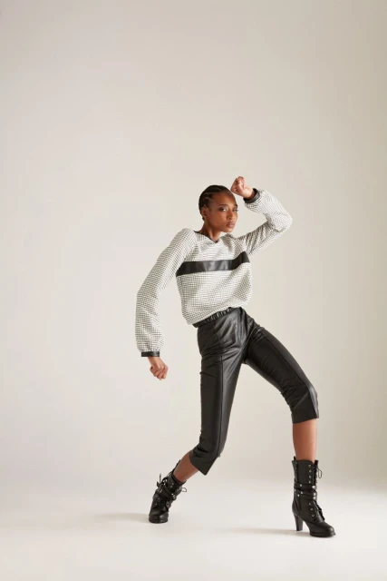 Woman in fashionable outfit posing in a studio. She's wearing a patterned top, leather-look culottes, and heeled boots against a neutral backdrop.