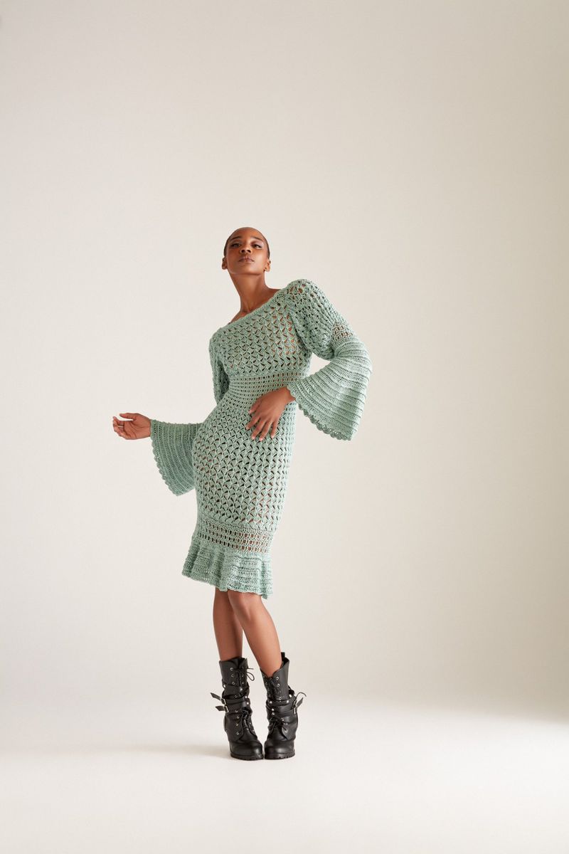 Elegant woman in a textured light blue midi dress and black buckled platform boots poses in a neutral-toned studio. Fashion editorial shot.