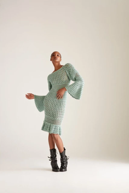 Elegant woman in a textured light blue midi dress and black buckled platform boots poses in a neutral-toned studio. Fashion editorial shot.