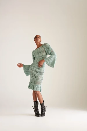 Elegant woman in a textured light blue midi dress and black buckled platform boots poses in a neutral-toned studio. Fashion editorial shot.