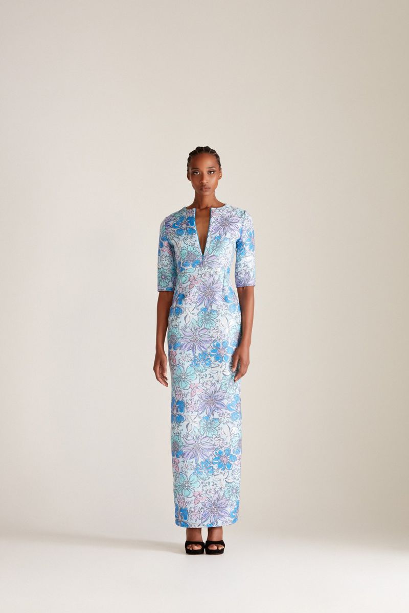 A single African-American woman stands in a studio wearing a floral-patterned dress and high heels in this full, eye-level shot.