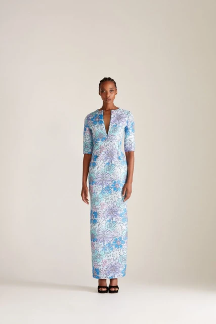 A single African-American woman stands in a studio wearing a floral-patterned dress and high heels in this full, eye-level shot.