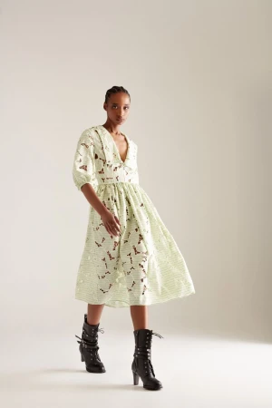Fashionable woman in a patterned dress and black boots poses confidently in a studio. Stylish, contemporary, and full-length shot.