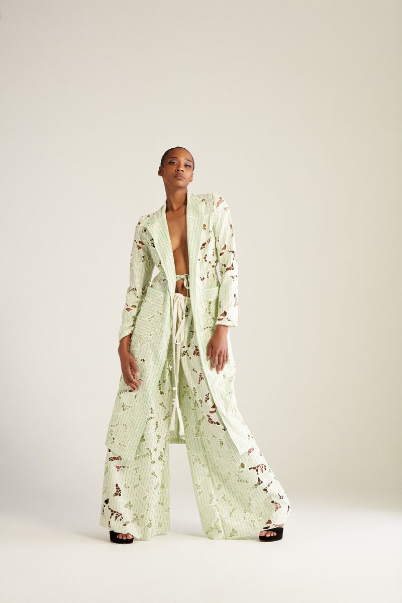 Fashionable adult woman poses in a light green patterned jacket and pants in a photo studio setting. Neutral backdrop and studio lighting.