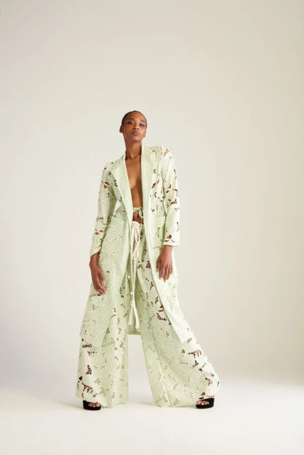 Fashionable adult woman poses in a light green patterned jacket and pants in a photo studio setting. Neutral backdrop and studio lighting.