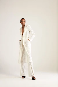 Model Goldie Carswell in a white textured coat and trousers standing against a white seamless background