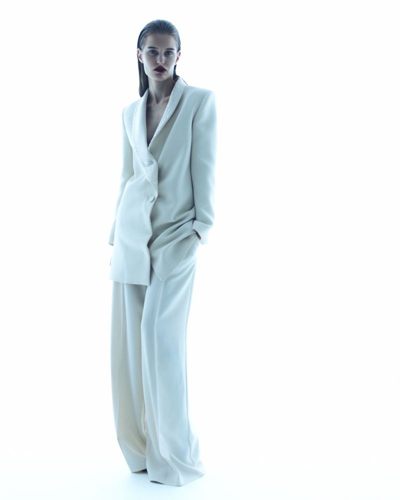 Elegant woman in a white blazer and pants, posing in a bright photo studio. Fashion editorial style with a modern, clean aesthetic.
