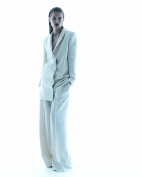 Model in an oversized cream tailored trouser suit with slicked-back hair standing against a pure white studio background.