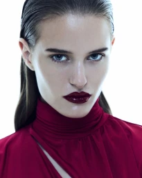 Close-up portrait of a woman with slicked-back hair and dark red lipstick wearing a crimson high-neck top against a white background.