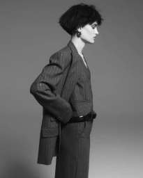 Model in pinstripe blazer and trousers posing against a grey studio background