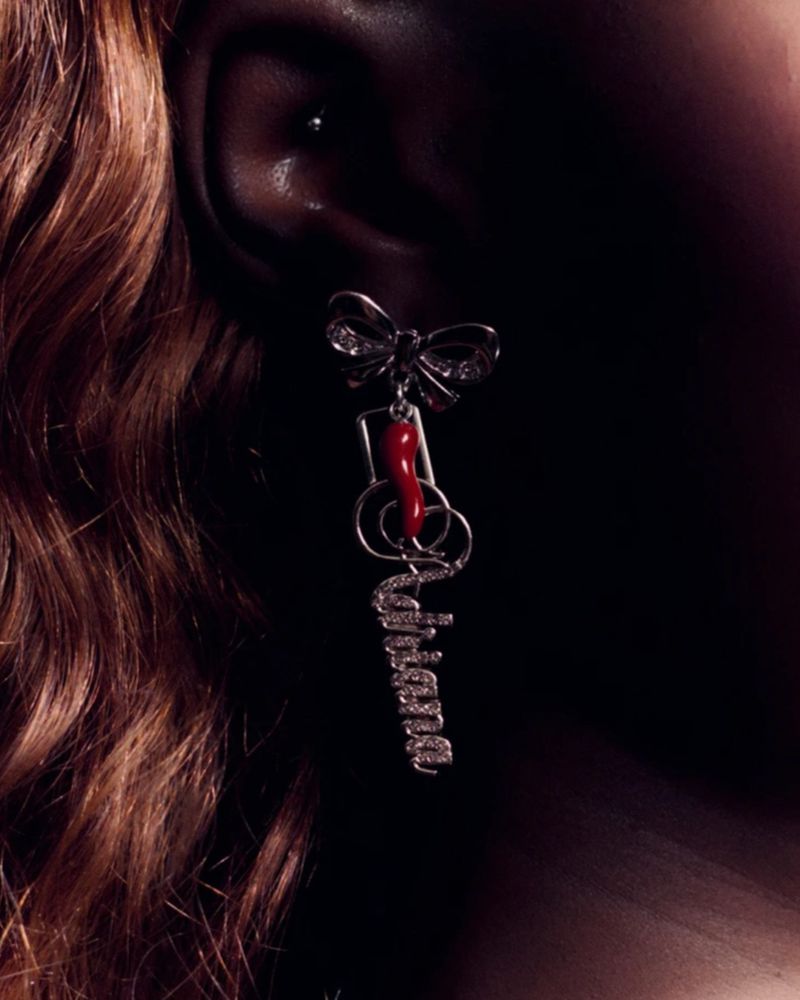Closeup of a woman's ear with a silver bow earring adorned with a red chili pepper and the word 'Ariana' in script.