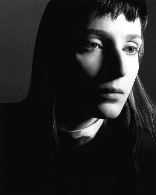 Black and white portrait of a young adult woman with dark hair, dramatic lighting, and a neutral facial expression in a photo studio.