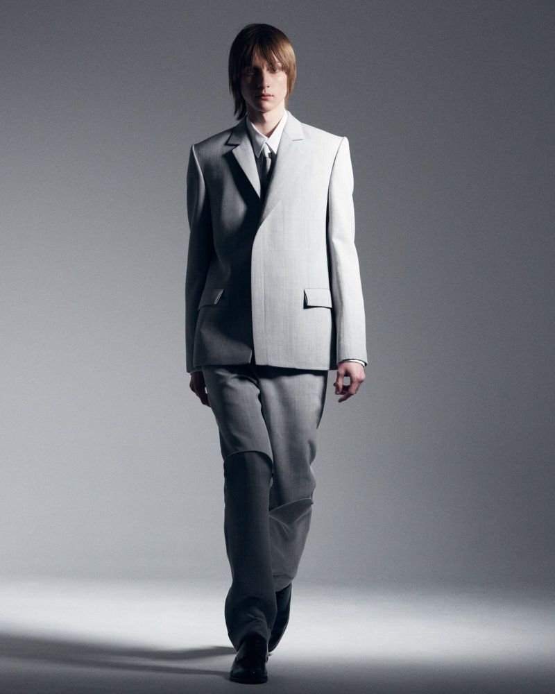 Man in a light grey suit walks forward in a studio setting with neutral gray background and modern, minimalistic style with soft lighting.