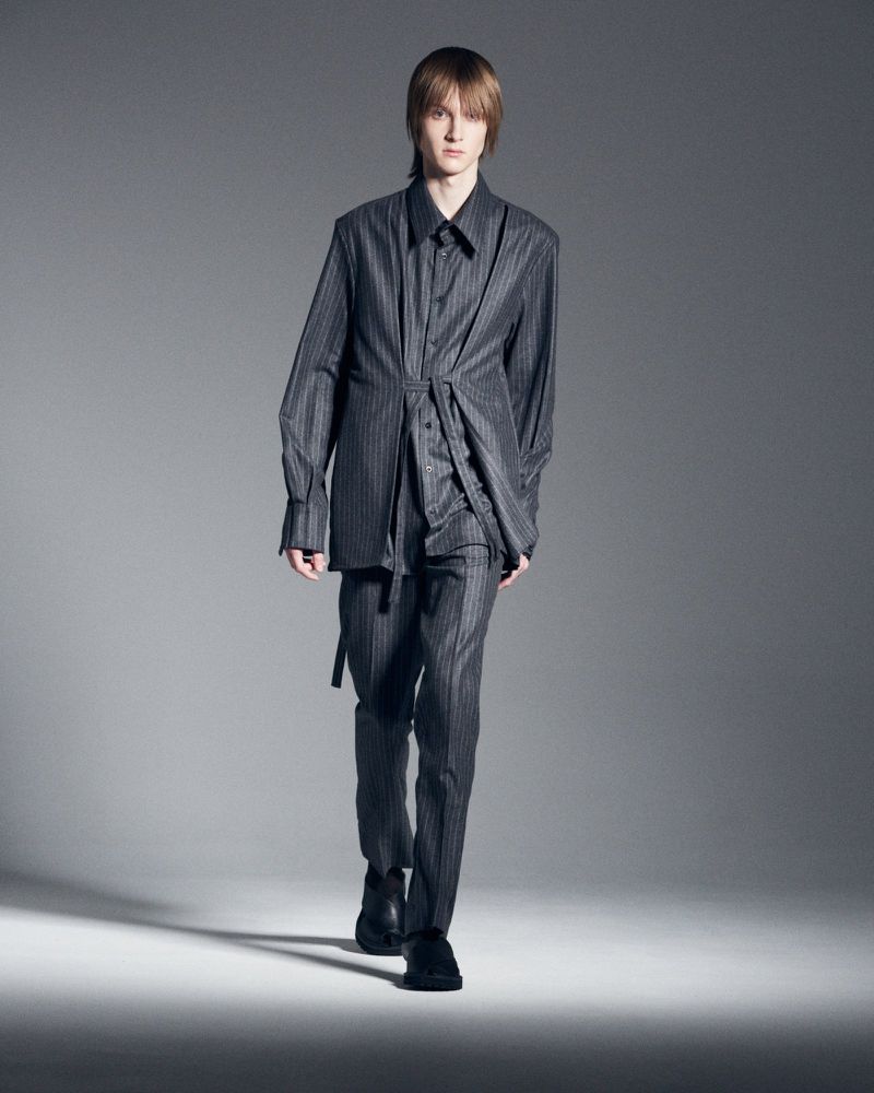 Male fashion model in gray pinstripe suit walking in photo studio against gray backdrop for a modern editorial fashion shoot.