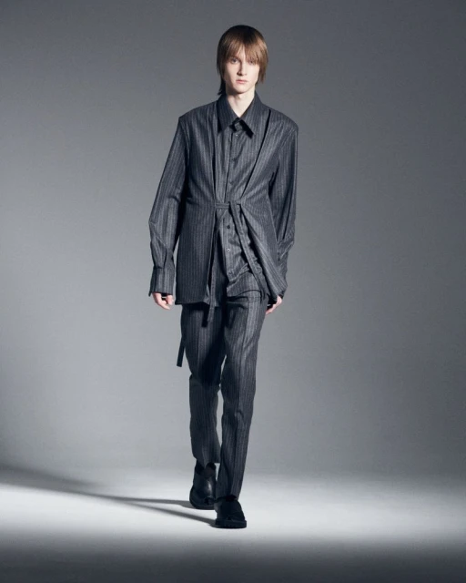 Male fashion model in gray pinstripe suit walking in photo studio against gray backdrop for a modern editorial fashion shoot.