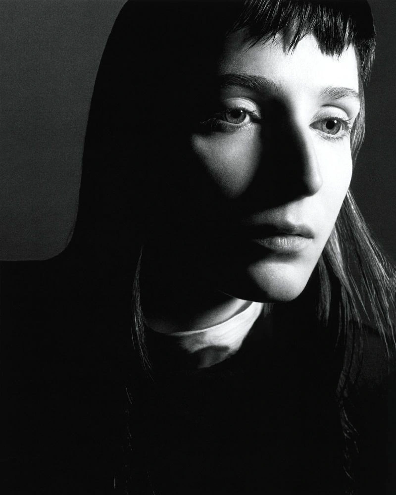 Black and white close-up portrait of a woman with short micro bangs illuminated by dramatic high-contrast shadow and light.