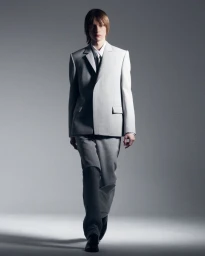 Model wearing a light grey tailored suit and tie against a neutral grey studio background.