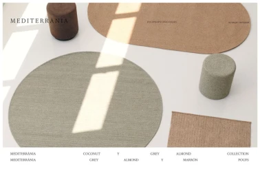 Overhead view of woven rugs in round and oval shapes arranged with cylindrical poufs on a white floor with angled sunlight shadows.