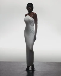 Model in a long white one-shoulder dress against a white studio background with dark flooring