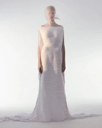 Model wearing a textured white floor-length gown with a sheer face veil against a seamless white studio background.