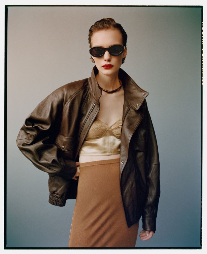 Model Penelope Ternes wearing an oversized brown leather jacket, bustier top, and dark sunglasses against a studio backdrop.