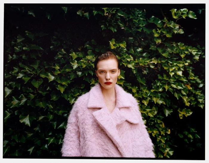 Model wearing a textured pink coat against a dense background of green leaves for Mytheresa Pre-Fall 2024.