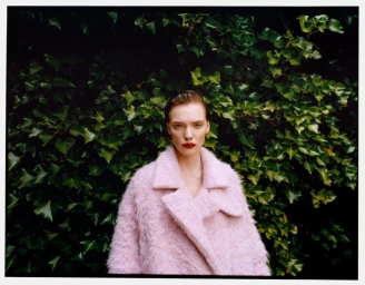 Model wearing a textured pink coat against a dense background of green leaves for Mytheresa Pre-Fall 2024.