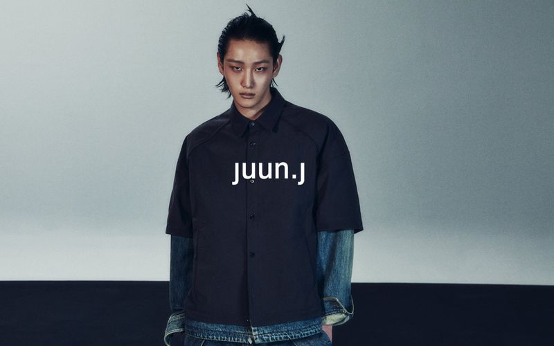 Asian male model wearing a black button-down shirt and denim jacket with text overlay 'juun.j' in a studio environment.