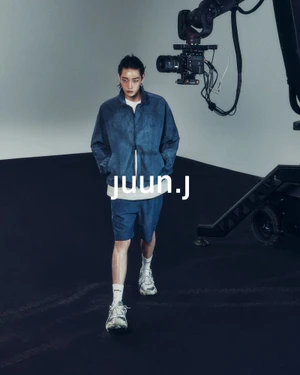 Model Hamin Yu walks in a blue denim zip jacket and matching shorts on a studio set next to a camera crane for Juun.J.