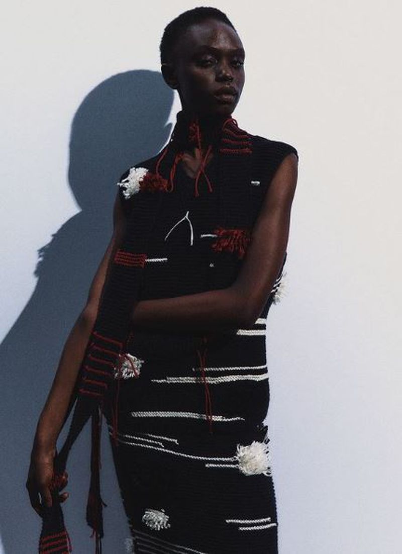 Fashion shot of an African-descent woman wearing a sleeveless black dress with white horizontal stripes and a black knitted scarf.