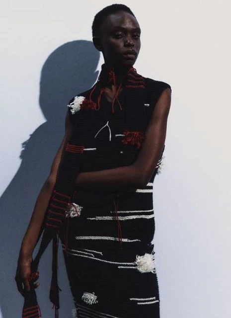 Fashion shot of an African-descent woman wearing a sleeveless black dress with white horizontal stripes and a black knitted scarf.