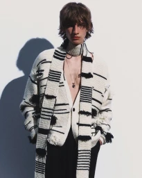 A male model wearing a textured cream and black striped knit cardigan and matching scarf against a white background.