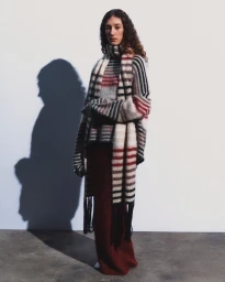 Model wearing a striped mohair knit sweater with matching fringe scarf and a long burgundy skirt against a studio wall.