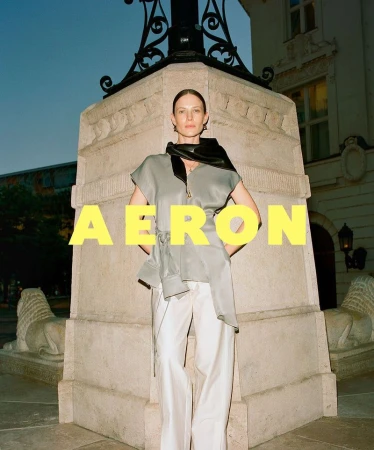 Fashion shot of a woman in a gray blouse and white pants posing in front of a stone structure with statues of lions in an outdoor setting.
