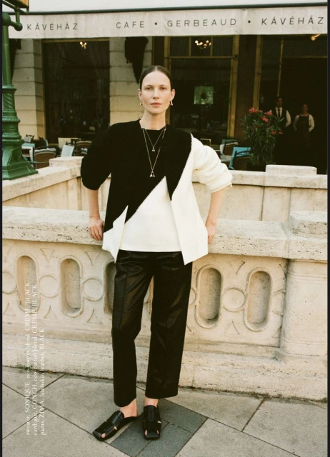 Woman in black and white sweater posing in front of Café Gerbeaud. She wears black pants and sandals, with natural light and urban setting.