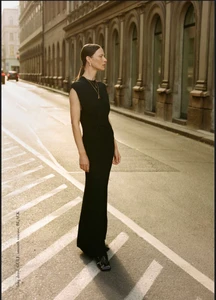 Model Angelika Wierzbicka in a sleeveless black viscose maxi dress standing on a sunlit European city street with arched facades.