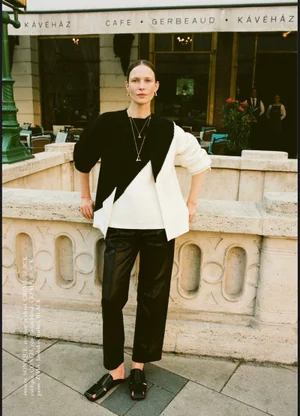 Model Angelika Wierzbicka standing outdoors wearing a black and cream color-block sweater and cropped black trousers.