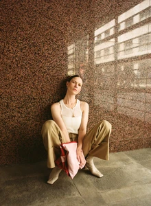 Model Angelika Wierzbicka sitting against a mottled granite wall wearing a white tank top, beige trousers, and boots.