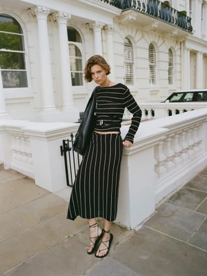 Model Bibi Breslin poses in a striped black knit top and matching midi skirt outside a white townhouse for Massimo Dutti.