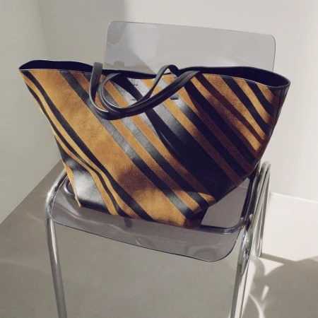 Phoebe Philo striped brown suede and black leather tote bag resting on a transparent acrylic chair.