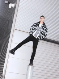 Model wearing a patterned black and white jacket posing against an industrial metal shutter wall for Balmain