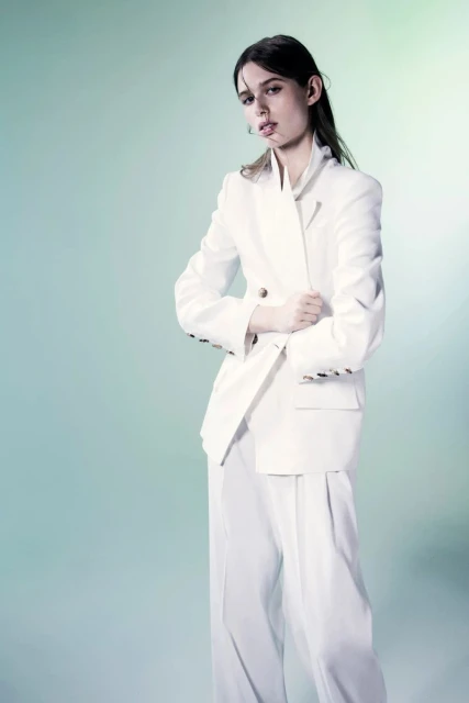 Fashion portrait of a young woman in an all-white double-breasted suit. Studio shot against a gradient light-blue background.