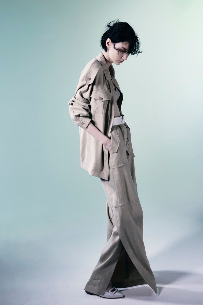 Woman in a khaki jacket and flared pants poses in a studio. Neutral colors and contemporary fashion create a chic editorial shot.